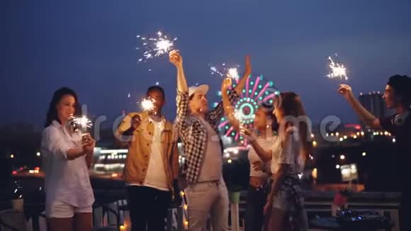 慢动作的快乐朋友燃烧孟加拉灯和跳舞在屋顶一起庆祝节日娱乐视频的预览图
