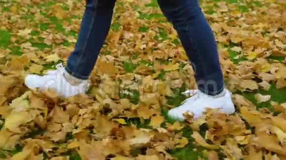 穿着白色运动鞋在秋叶上行走的时髦的脚视频的预览图