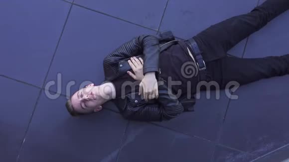 苗条的金发年轻白种人穿着黑色夹克躺在瓷砖地板上唱歌视频的预览图