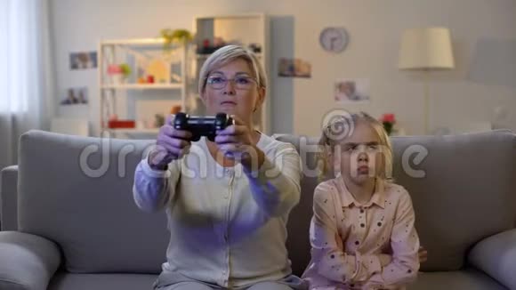 兴奋的奶奶玩电子游戏无视悲伤的孙子坐沙发成瘾视频的预览图