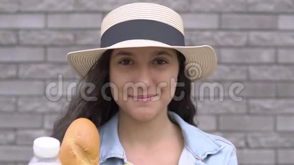 年轻漂亮的女人穿着牛仔夹克和帽子拿着一个包装产品有一个好心情和微笑视频的预览图