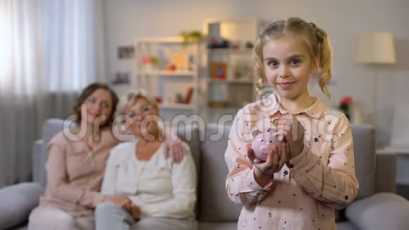 女学生把硬币放在储蓄罐里骄傲的母亲和奶奶在后面储蓄视频的预览图