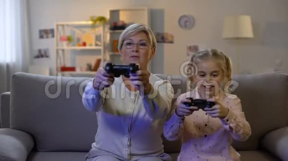 可爱的女孩和现代奶奶在家玩电子游戏与操纵杆休闲视频的预览图
