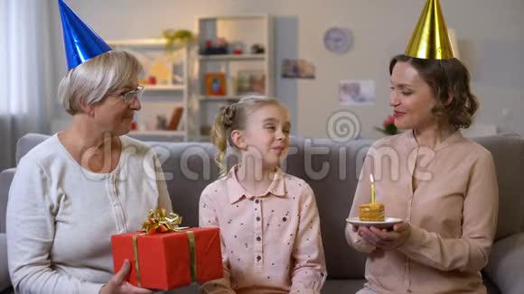 可爱的妈妈和奶奶祝贺可爱的女孩生日吹蜡烛视频的预览图