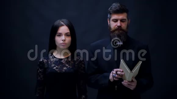 穿着黑色衣服的女孩和牧师在黑色背景下接受洗礼牧师在黑色背景上祈祷宗教修女视频的预览图