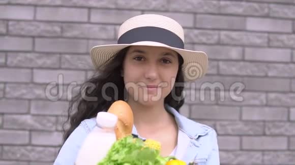 穿着牛仔夹克和帽子的年轻漂亮女孩拿着一个包裹里面的产品心情很好微笑着视频的预览图