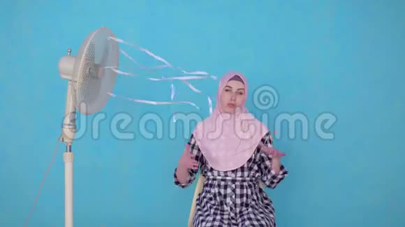 戴头巾的年轻穆斯林妇女在炎热的天气中被风扇冷却视频的预览图