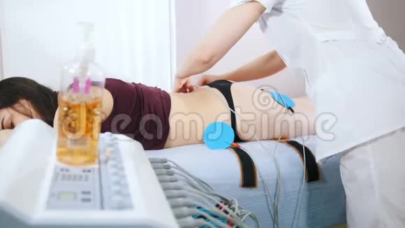 美容诊所年轻女子在床上打肌刺激一位医生把一个设备连接到身体上视频的预览图