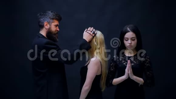 牧师保佑姑娘们宗教概念黑胡子男人和两个女孩在黑色背景上祈祷宗教是视频的预览图