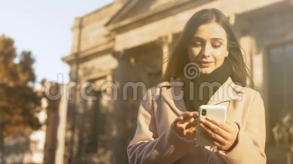 年轻女士在漂亮的古典建筑附近的智能手机上滚动银行应用程序视频的预览图