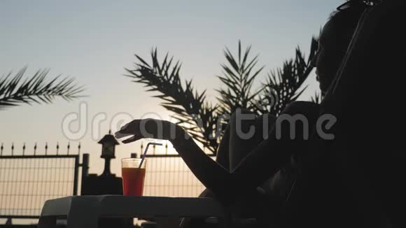 剪影年轻女子在日落时在海滩上喝鸡尾酒视频的预览图