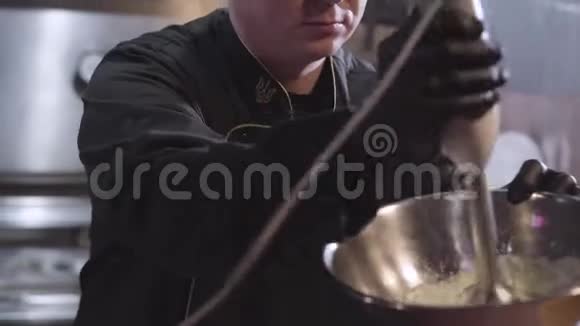 厨师穿着制服和黑色橡胶厨师手套用搅拌机在大铝碗里搅拌准备食物视频的预览图