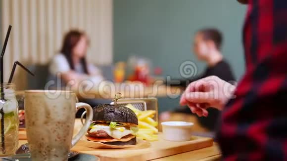 一对夫妇坐在一家咖啡馆的桌子旁侍者端着菜两个黑色汉堡视频的预览图