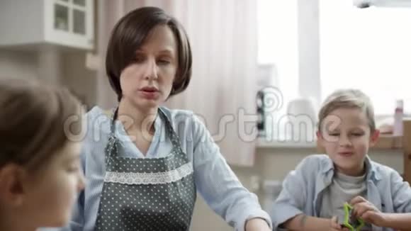 妈妈和孩子们一起在厨房的桌子上擀面皮做饼干同时他们也在近距离讲述故事视频的预览图