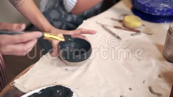 女艺术家正在车间的桌子上用黑色染料着色新的粘土杯视频的预览图