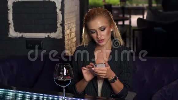 晚上酒吧里一个女孩带着电话和一杯红酒的肖像视频的预览图