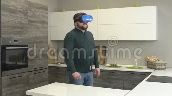 一个戴着虚拟现实眼镜的时髦男人在一个现代化的厨房里散步慢动作美食视频的预览图