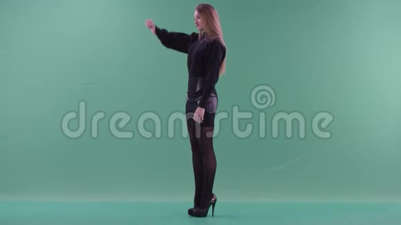 一位身穿黑色休闲服的年轻漂亮女子正竖起大拇指侧身站在绿色的屏幕上视频的预览图
