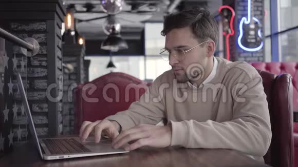 帅哥在现代咖啡馆里用笔记本电脑工作时尚自信的商人思考解决问题视频的预览图
