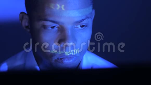 程序员或黑客寻找监控软件代码反映在他的脸上一个黑人男人在黑暗的房间里视频的预览图