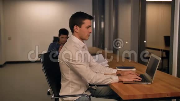 英俊的年轻人写在笔记本上看办公室里的显示器而不是看相机视频的预览图