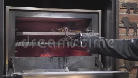 用黑色橡胶手套做饭用金属工具把一块肉放在烤箱里用火把厨师推鲜多汁的视频的预览图