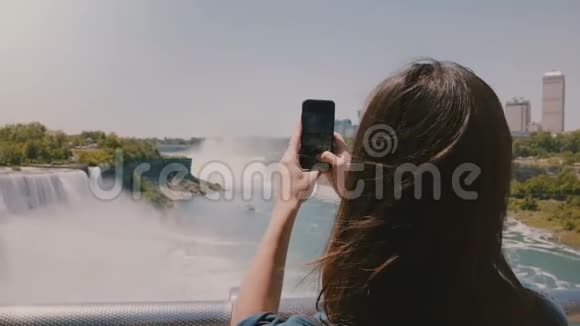 美丽的慢镜头后景拍摄年轻的年轻旅游妇女拍摄不可思议的尼亚加拉瀑布全景视频的预览图