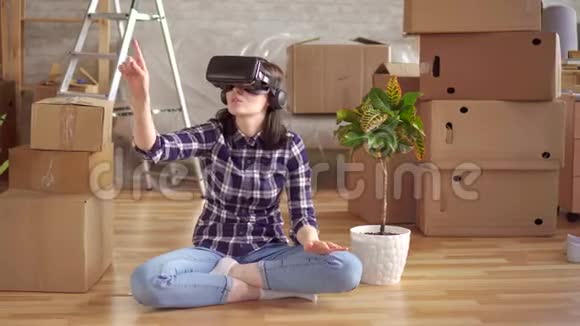 一位戴着虚拟现实眼镜的年轻女子坐在盒子旁边的地板上的画像视频的预览图