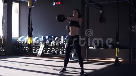 穿着运动服的健身女孩穿着10公斤水壶铃做交叉健身运动头部以下的高度提升视频的预览图