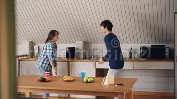 穿休闲服装的快乐女孩和男人在现代公寓的厨房里跳舞和欢笑放松和享受乐趣视频的预览图