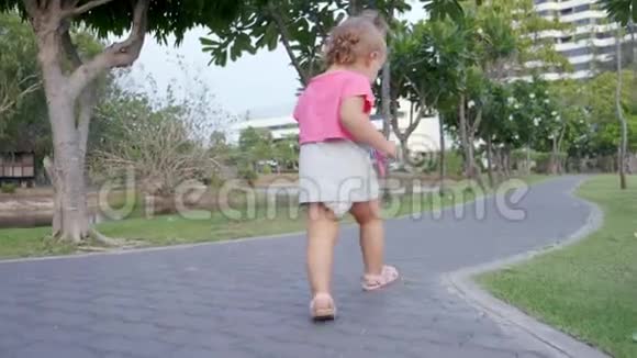一岁的小女孩沿着公园里的一条小径在棕榈树之间奔跑动作缓慢4K视频的预览图
