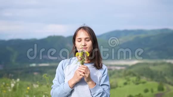 年轻漂亮的黑发女人在田野里捧着一束野花漂亮的女孩嗅着鼻子向前伸展花朵视频的预览图