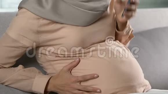 戴头巾的孕妇用电话紧急呼叫宫缩视频的预览图