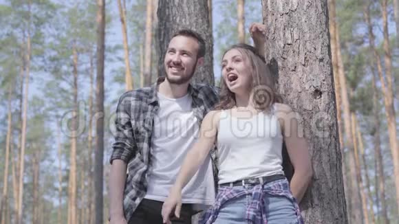 英俊的年轻人和漂亮的女人站在松林里看着远处的肖像露营的概念休闲视频的预览图