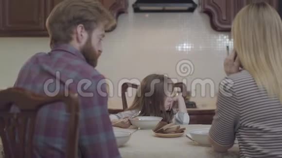 年轻的女人和男人坐在桌子旁吃早餐这位女士用手机聊天然后和男人讨论工作视频的预览图