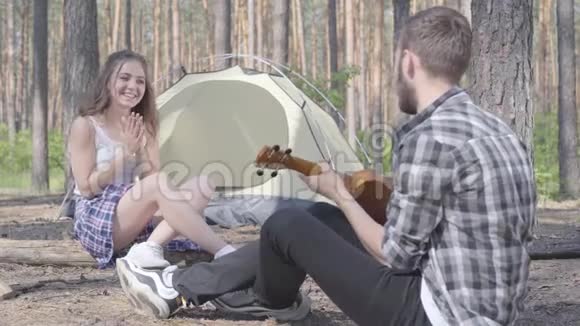 那个年轻人在帐篷里玩四弦琴而漂亮的年轻女人坐在他面前拍手可爱的一对视频的预览图