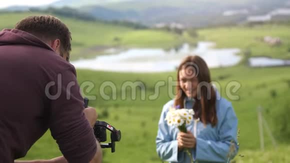 游客夫妇享受大自然年轻人拍照快乐的女人拿着一束田野的花慢动作视频的预览图