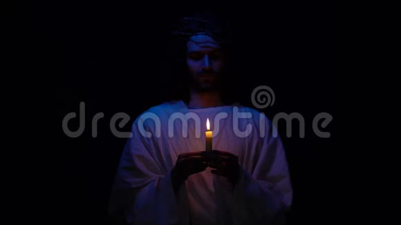 戴着荆棘王冠的基督教圣徒在黑暗中拿着蜡烛为人们祈祷视频的预览图
