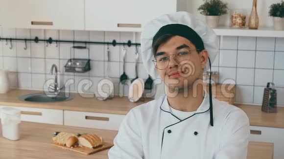 厨房里男人的肖像年轻的成年人穿着白色的帽子和制服做饭视频的预览图