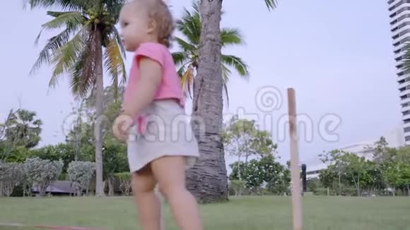 一岁的小女孩在公园的一片绿色草地上奔跑在棕榈树之间动作缓慢视频的预览图