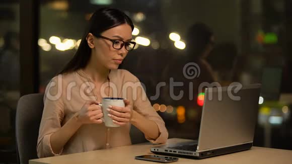 令人不安的女人在电脑上打字晚上喝咖啡上班工作狂视频的预览图