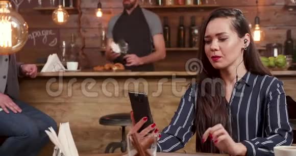 时尚漂亮的女人使用她的智能手机和耳机同时从事视频通话视频的预览图