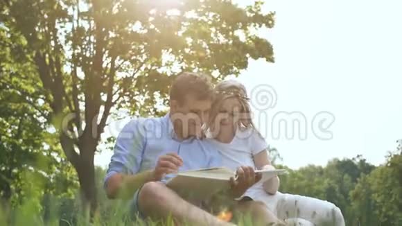 一个男人和一个女孩正在看一张家庭相册里面有草地上公园里的照片视频的预览图