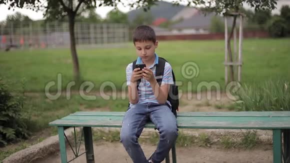 小男孩背着背包坐在长凳上课间玩网络游戏视频的预览图