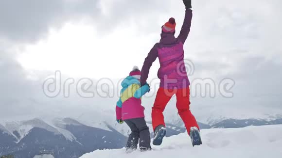 母亲和女儿享受旅程在滑雪场穿着冬装的幸福家庭冬天的时候看着视频的预览图