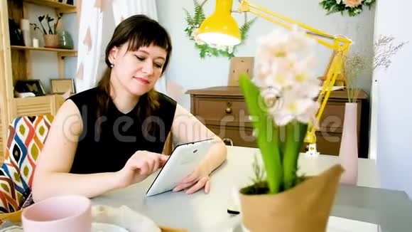 年轻女子在家里的餐桌上休息时使用平板电脑视频的预览图