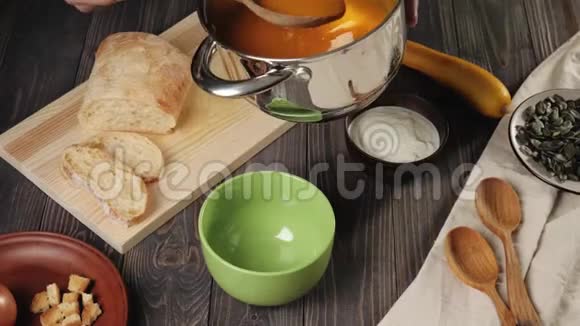 奶油南瓜汤烹饪厨师把奶油南瓜汤放在装饰好的木桌上的绿色碗里4K视频的预览图