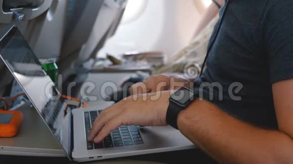 年轻的自由职业商人带着智能手表在飞机商务旅行飞行中使用笔记本电脑在线工作视频的预览图