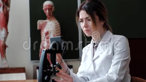 一个女人坐在教室的显微镜后面视频的预览图