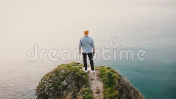 镜头旋转周围年轻快乐的白人男子站在史诗般的日落海景诺曼底岩石海岸悬崖顶部视频的预览图